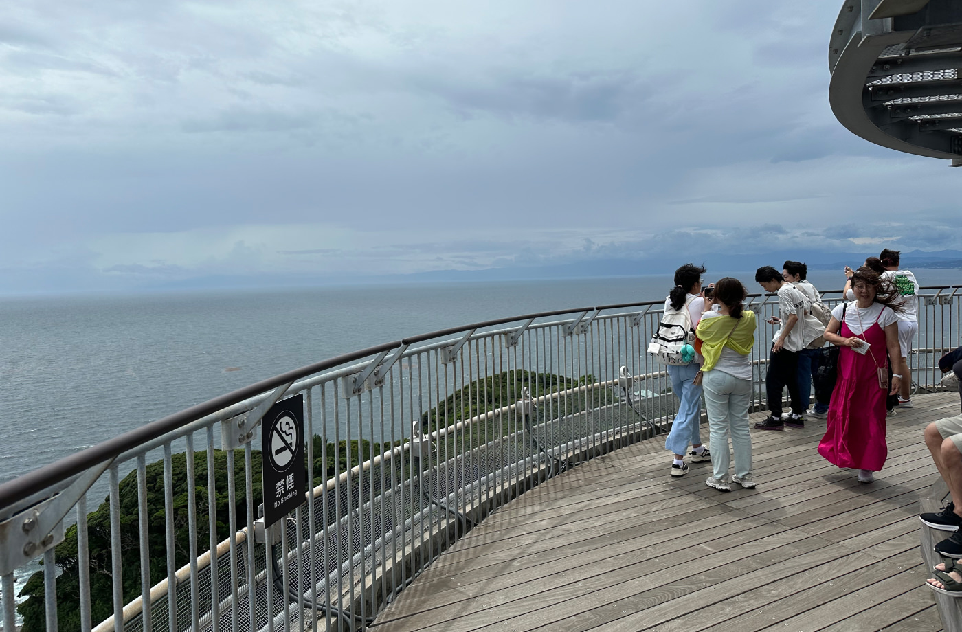 Utsikt över havet på en rund träterass med stålräcke uppe på ett observatorium. Flera tittar och fotograferar utsikten.