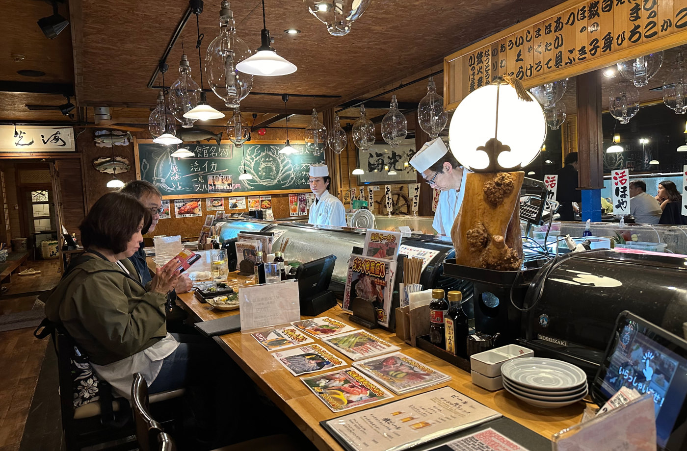 Mysig bardisk, vilken två kockar står bakom och lagar mat. Dekoren i restaurangen är gjord av trå och det finns många taklampor.