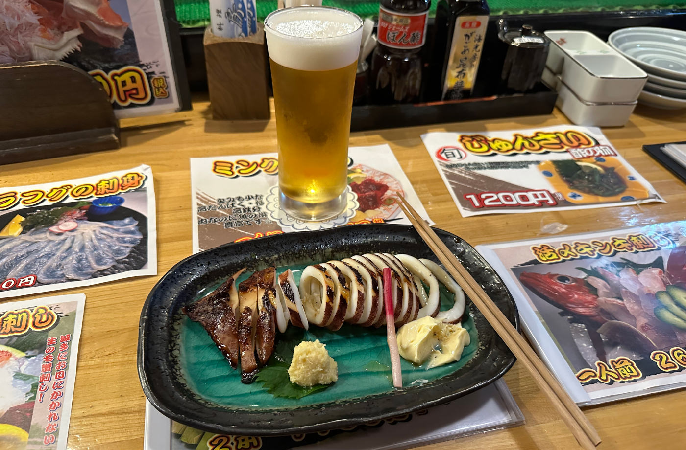 Bardisk med en mörk tallrik med skivad grillad bläckfisk och mald pepparrot och majonäs. Även ett stop öl.