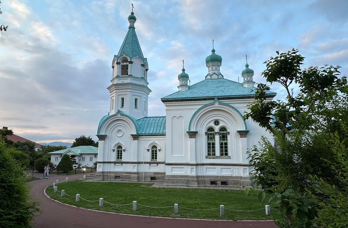 Gammal rysk ortodox kyrka med liten rund gräsmatta. Kyrkan är vit med ljusblått tak.