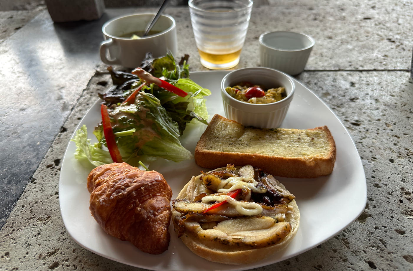 Frukostallrik med sallad, bröd, croissant och en liten skål. Även soppskål och glas med juice.