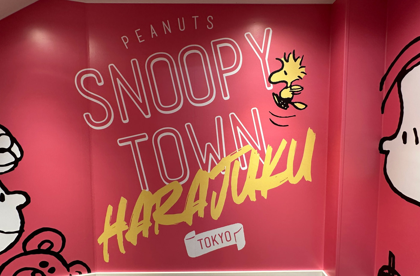 Väggmålning i varuhus. Väggen är rosa och texten är vit och lyder "Peanuts Snoopy Town Harajuku Tokyo".