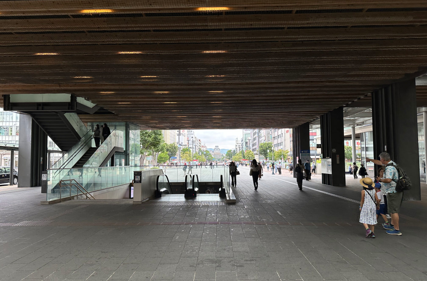 Utomhusdel av en tågstation under tak. Till vänster syns vanliga trappor och en rulltrappa. I fjärran en bred gata med höga hus och ett slott mot slutet av den.