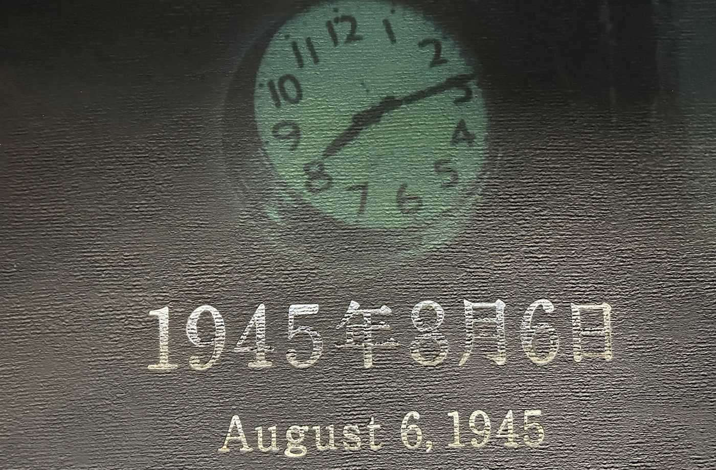 Väggmålning med en klocka som visar tiden 08:15. Under står texten "August 6, 1945". Texten är vit, väggen grå och klockan ljusgrön.