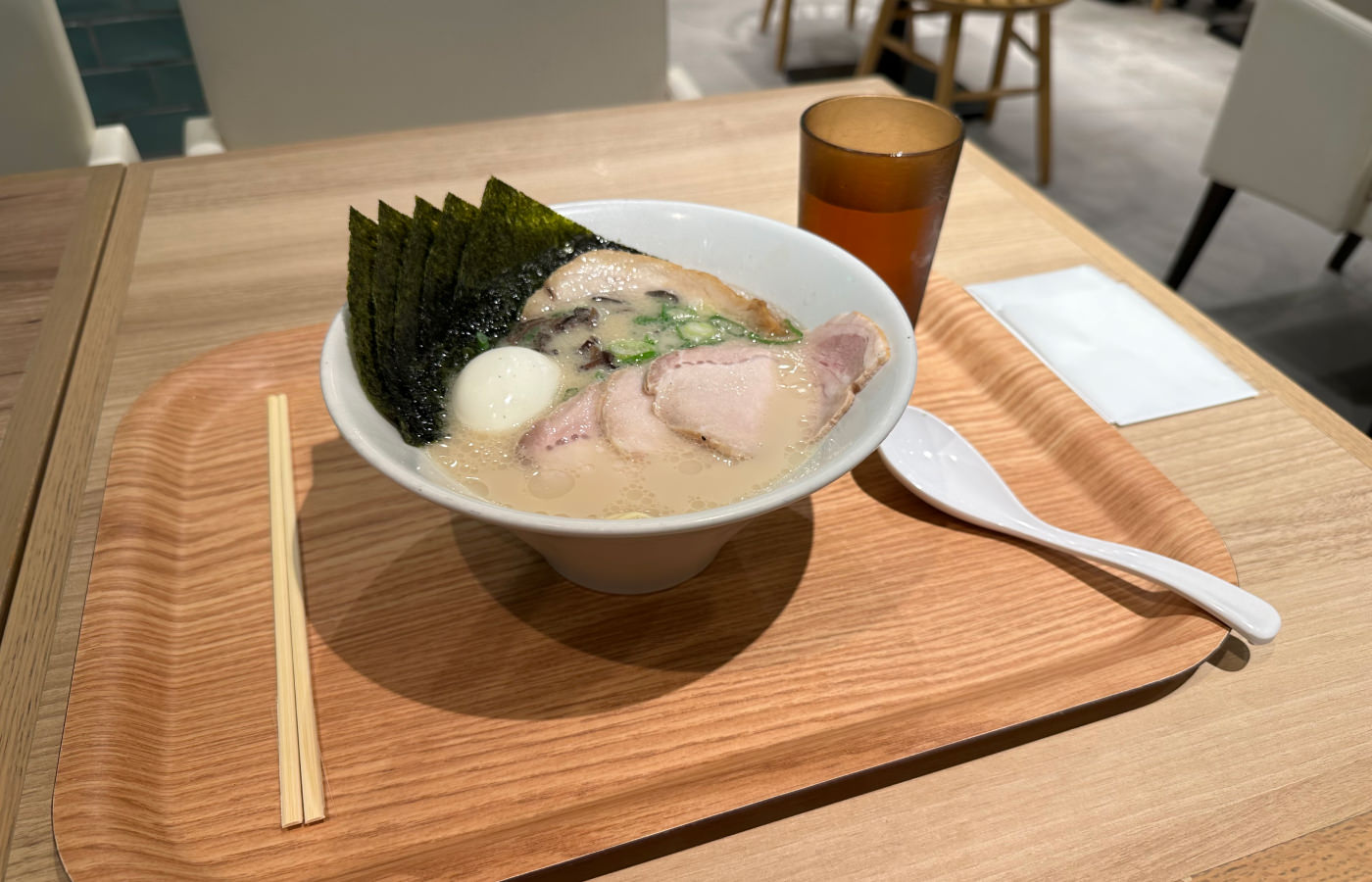 En våt skål med ramen med ljus sky på en träbricka på ett träbord.