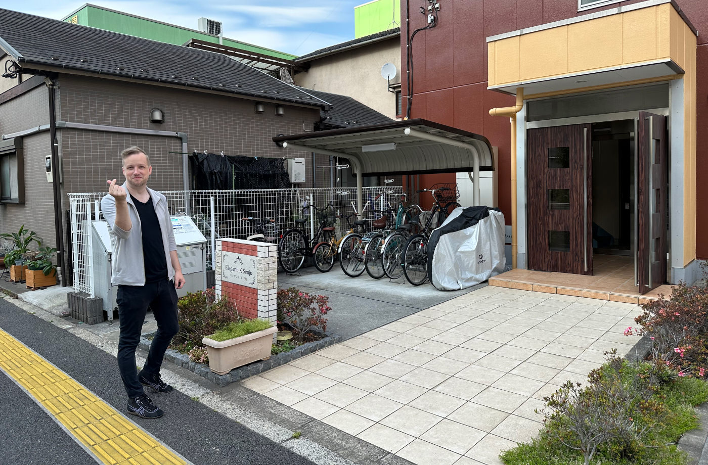 Västerländsk man i svarta kläder står framför ingången till ett hus poserar.