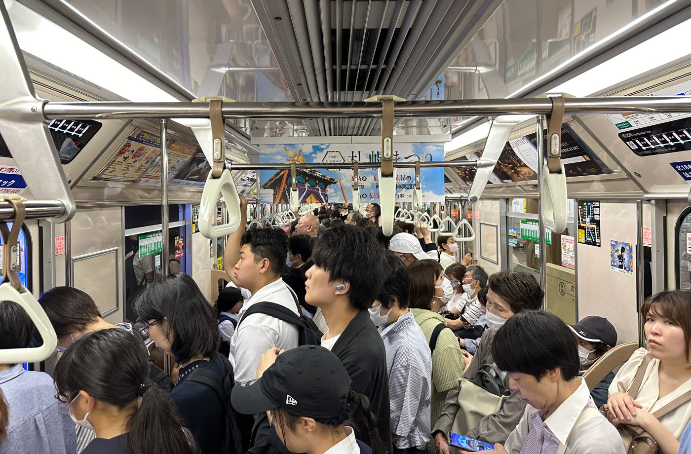 Lång och proppfull tunnelbanevagn. Alla är japaner och har mörkt hår.