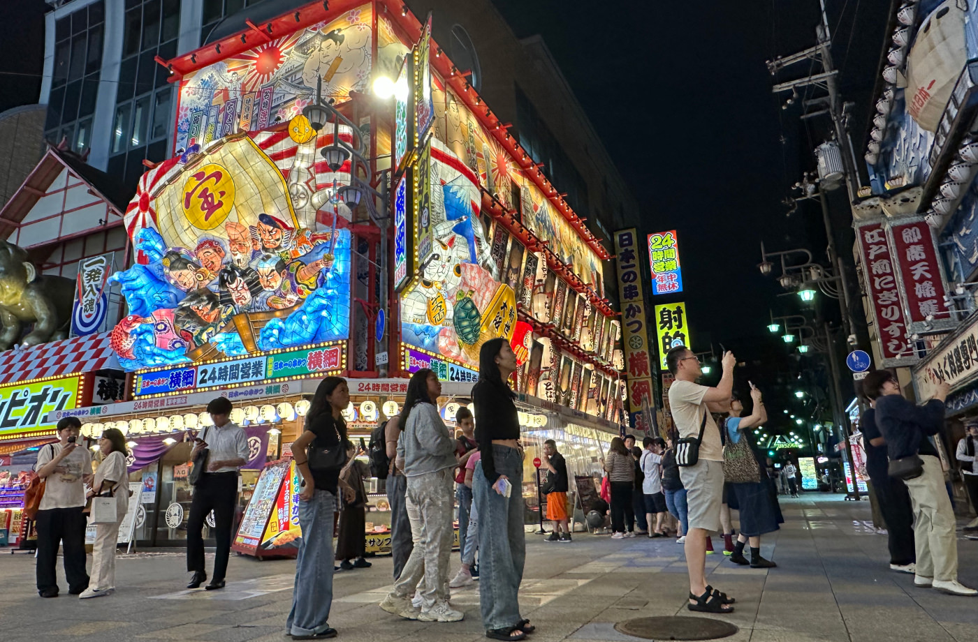 Restaurang med enormt upplyst tredimensionell skylt på sin fasad. Skylten innehåller japanska figurer.