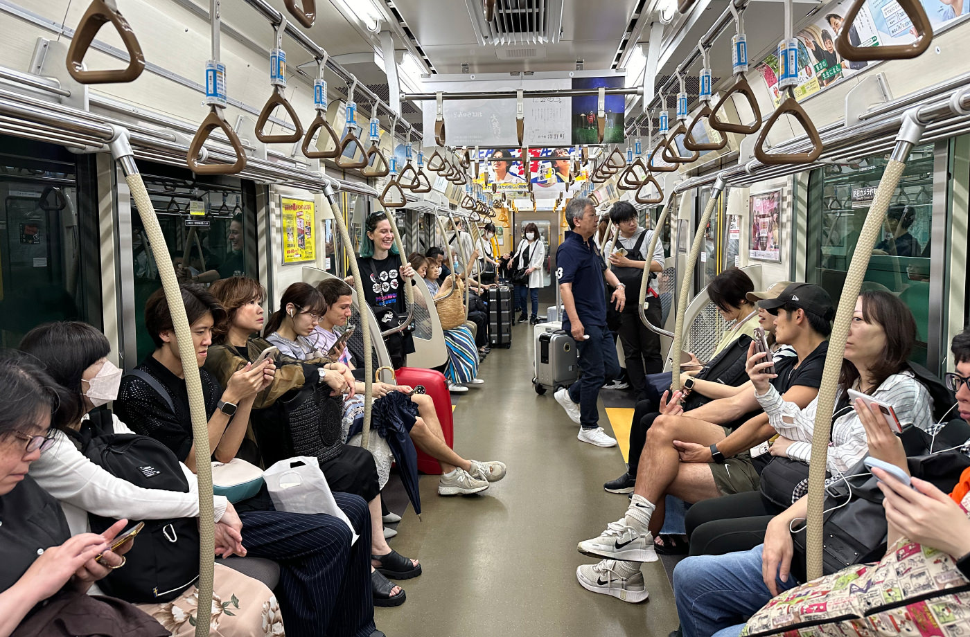 Full tunnelbanevagn i Tokyo där folk sitter på varje sida. Några har med stora väskor.